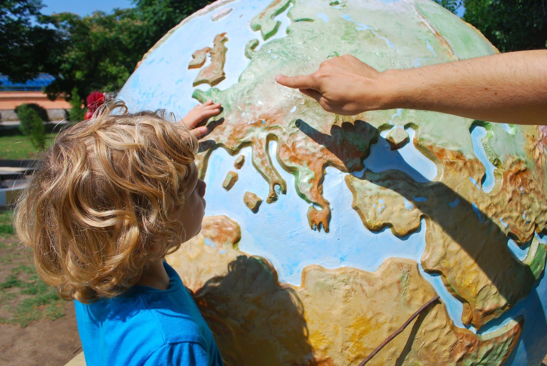 Un enfant pose la main sur un grand globe terrestre en relief qu'un adulte lui montre du doigt